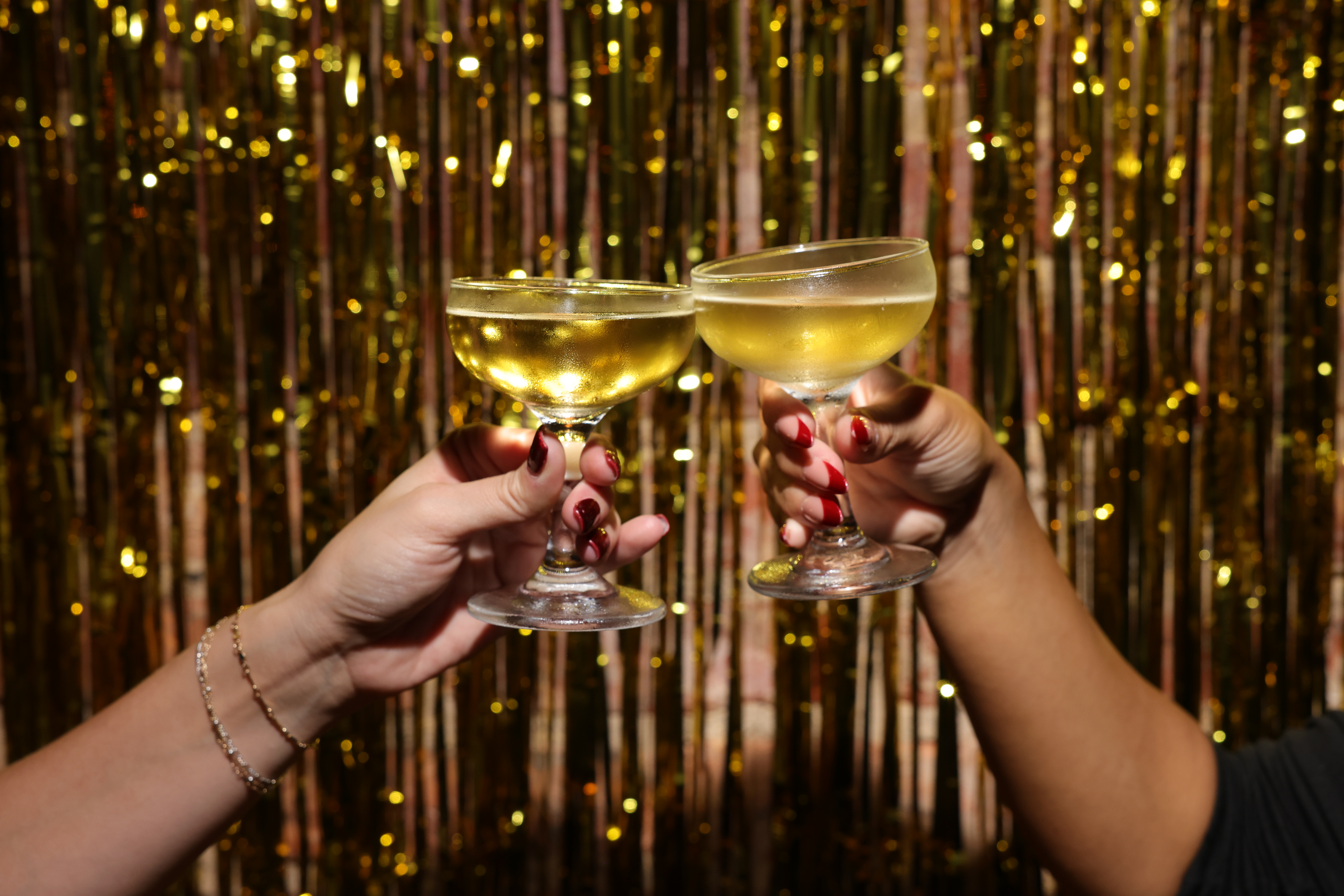 Two champagne coupes clinking in a toast against a gold tinsel backdrop